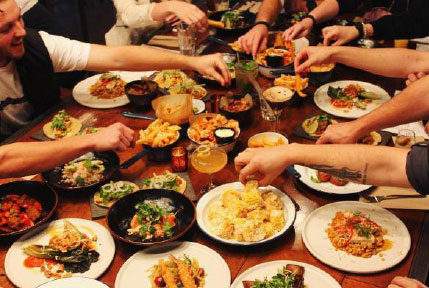 Large feast on restaurant table with people helping themselves to food.