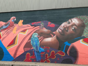 Mural of dark skinned woman reclining with colourful clothes and parrots