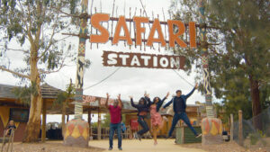 Four adults jumping under the sign 'Safari Station'